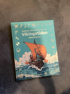 Vikingatiden av Fabian Göranson - Upptäck Sveriges fantastiska historia med boken 'Vikingatiden' av Fabian Göranson. Boken har ett turkost hårdband med illustration av ett vikingaskepp och guldiga symboler runtom. Perfekt för dig som gillar äventyr och historia.Obs går att upphämtas i södra Stockholm 