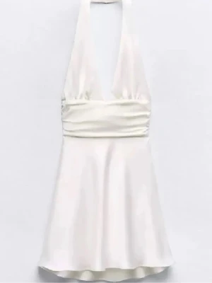 Vit kort satin klänning med öppen rygg - Supersnygg vit kort klänning i satin med halterneck och djup v-ringning. Klänningen har markerad midja och ett glansigt, slätt tyg som ger en lyxig känsla. Med öppen rygg. Perfekt för sommarens alla tillfällen!