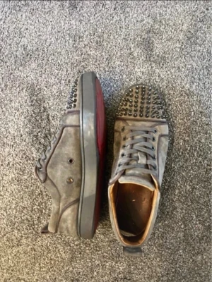 Gröna Louboutin sneakers med nitar - Säljer ett par gröna sneakers från Christian Louboutin med coola svarta nitar på tån och sidorna. Skorna har klassisk röd sula, snörning och är gjorda i mocka. Perfekta för dig som vill sticka ut med en edgy stil.