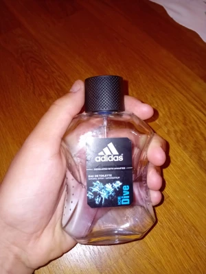 Adidas Ice Dive Eau de Toilette - Fräsch parfym från Adidas, Ice Dive Eau de Toilette. Flaskan är genomskinlig med en svart, räfflad kork och har en sportig design. Etiketten är svart med blå detaljer och visar en isblå grafik. Perfekt för dig som gillar en energisk och uppfriskande doft.