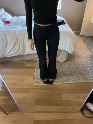 Mörkblå bootcut jeans - Säljer ett par mörkblå bootcut jeans med hög midja och klassisk femficksdesign. Jeansen har en snygg utsvängd passform nedtill och är tillverkade i ett stretchigt denimtyg som sitter bekvämt. Perfekta för dig som gillar en tidlös och trendig look.