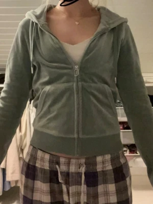 Juicy tröja - Mysig grön hoodie i mjuk velour med dragkedja framtill och fickor. Tröjan har huva och ribbade muddar vid ärmslut och nederkant. Har en fläck från färg på insidan av tröjan men inget som syns när man har på sig den.