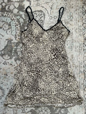 Leopardmönstrad mini dress med smala band - Säljer en klänning med leopardmönster i svart och beige. Modellen har smala axelband och v-ringad hals med svarta kantdetaljer. Materialet känns lätt och svalt.