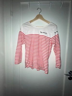 Randig långärmad topp från Bondelid - Säljer en vit och röd långärmad topp från Bondelid med klassiskt randigt mönster. Toppen har rund halsringning och broderad Bondelid-logga på bröstet samt två små stjärnor på axeln. Perfekt för en avslappnad och stilren look. Den har små små håll i mitten.
