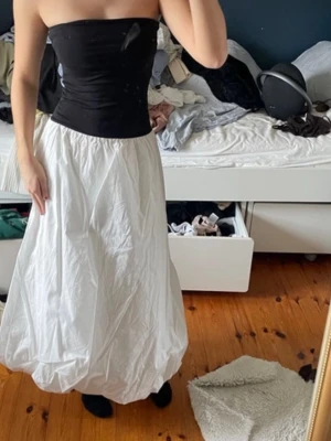 Vit långkjol med ballongform - Säljer en vit långkjol med ballongformad siluett. Kjolen har en enkel och luftig design som ger en cool och avslappnad vibe. Perfekt att styla med crop tops eller stickade tröjor för en trendig look.