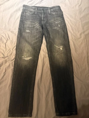 Grå slitna jack and Jones jeans slim fit - Säljer ett par grå jack and Jones jeans med snygga slitningar på låren och knäna. Modellen är slim fit och endast använda en gång så som nya.