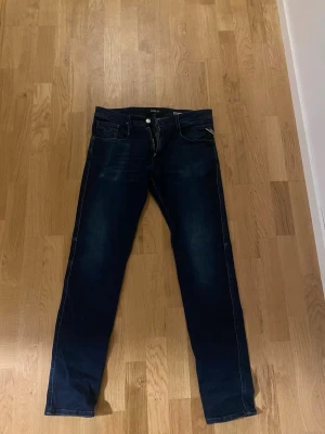 Mörkblå anbass jeans från Replay - Snygga mörkblå jeans från Replay med raka ben och klassisk femficksdesign. Jeansen har diskreta slitningar och kontrastsömmar som ger en cool look. Tillverkade i ett mjukt denimtyg som sitter skönt hela dagen. Slim fit L34 W33