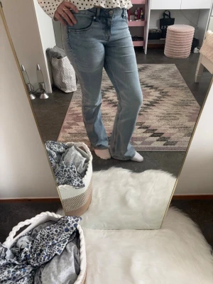 Ljusblå låg midjade utsvängda jeans - Säljer ett par ljusblå jeans med utsvängd passform och klassisk femficksdesign. Jeansen har låg midja och stängs med knapp och dragkedja. Perfekta till en avslappnad och trendig look. Materialet är denim i bomull.