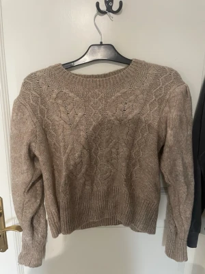 Beige kabelstickad tröja KappAhl - Säljer en beige kabelstickad tröja från KappAhl. Tröjan har rund halsringning, ribbstickade muddar och nederkant samt ett klassiskt flätmönster framtill. Perfekt för lager-på-lager och riktigt mysig under kyliga dagar.