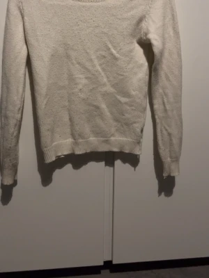 Vit stickad tröja med rund hals - En enkel och stilren vit stickad tröja med rund hals och långa ärmar. Tröjan har ribbstickade muddar vid ärmslut och nederkant. Perfekt att matcha med jeans eller kjol för en clean look.