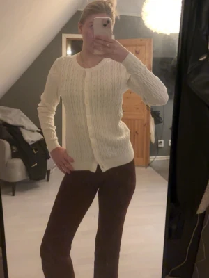 Vit kabelstickad kofta Basic You - Säljer en vit kabelstickad kofta från Basic You i ekologisk bomull. Koftan har rund hals, knappar framtill och ribbade muddar. Perfekt för lager-på-lager och enkel att matcha med olika outfits. Bara använd fåtal gånger, köpt på ullared.