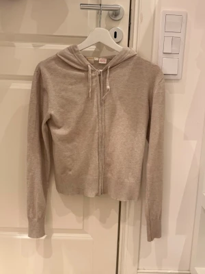 Beige ziphoodie med huva - Säljer en beige ziphoodie från Brandy Melville. Hoodien har dragkedja framtill, långa ärmar och en justerbar huva med snören. Modellen är croppad och tillverkad i mjukt bomullsmaterial, perfekt för en avslappnad stil.
