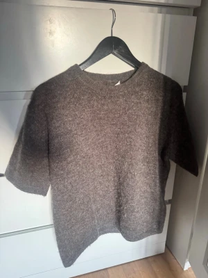 Grå stickad t-shirt  - Mysig grå stickad t-shirt med korta ärmar och rund halsringning. Tröjan har en avslappnad passform .Perfekt för lager-på-lager och enkel att styla till olika outfits.