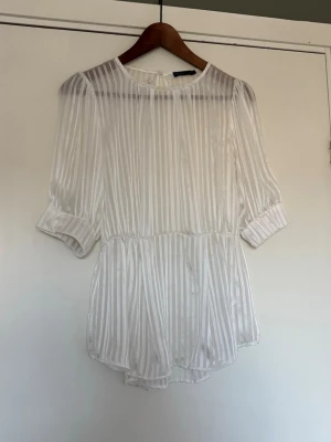 Vit transparent blus med ränder - Snygg vit blus från Bik Bok med transparent tyg och vertikala ränder. Blusen har rund halsringning, halvlånga puffärmar och knäppning i nacken. 