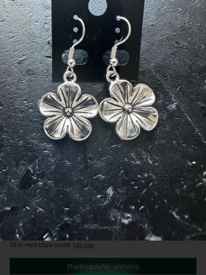 Silvriga blomformade örhängen - Säljer ett par snygga örhängen i form av blommor i silverfärgad metall. De har en tydlig blomdesign med fem kronblad och en liten detalj i mitten. Perfekta för att ge din stil en cool och unik touch.