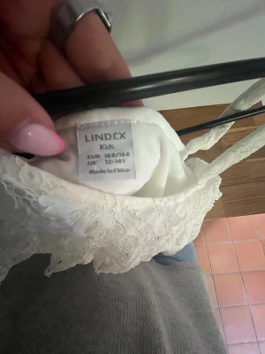 Skolavslutningsklänning - Säljer en vit kort spetsklänning från Lindex med oneshoulder-design och smal axelrem. Klänningen har en romantisk känsla med volangdetalj upptill och är perfekt för sommarens alla tillfällen. Inga fläckar eller hål!