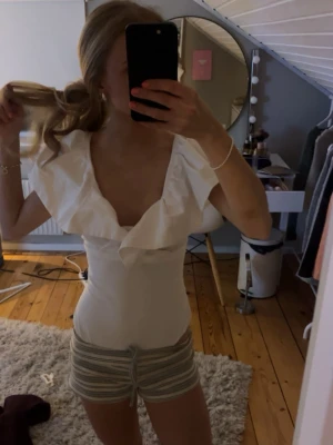 Vit volang body med djup v-ringning - Säljer en vit body med volangdetaljer och djup v-ringning. Blusen är ärmlös och har en slim passform.