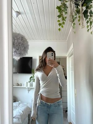 Ljusgrå omlottopp med knyt - Säljer en ljusgrå omlottopp med v-ringning och knyt i sidan. Mjukt och skönt material, aldrig kommit till användning!(Säljer även jeansen i tidigare annons)