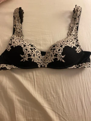 Intimissimi push-up Svart spets-bh med vit brodyr - Snygg svart bh med vit spetsbrodyr och blommigt mönster. Bh:n har vadderade kupor och breda axelband med spetsdetaljer. Perfekt för dig som gillar en elegant och feminin stil. Materialet är mjukt och bekvämt mot huden.