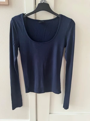 Mörkblå långärmad topp Gina Tricot - En enkel och stilren mörkblå långärmad topp från Gina Tricot. Toppen har en djup rundringning och är tillverkad i ett mjukt bomullsmaterial som sitter skönt mot kroppen. Perfekt att matcha med jeans eller kjol för en clean look. Säljer den då den är lite för stor