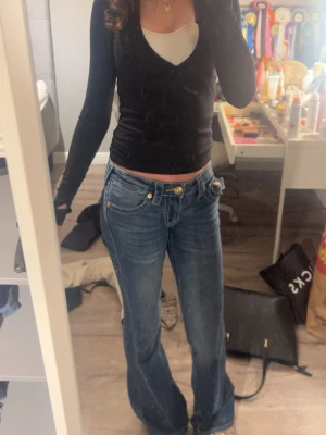 True Religion Jeans - Säljer ett par blå bootcut jeans från True Religion i storlek W24 som är knappt använda med klassiska kontrastsömmar och guldiga detaljer på fickorna. Jeansen är väldigt lowaist och en snygg passform som framhäver benen.