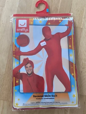 Röd Second Skin Suit från Smiffys - Säljer en helkroppsdräkt i röd färg från Smiffys, perfekt för maskerad eller cosplay. Dräkten är tight och täcker hela kroppen inklusive ansiktet, med dragkedja och stretchigt material som ger en slimmad look.