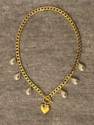 Guldhalsband med pärldroppar och hjärta - Snyggt halsband i guldfärgad rostfritt stål med fem droppformade pärlor och ett hjärtformat hänge. Kedjan har en chunky design och stängs med en toggle-lås. Perfekt för dig som vill ha något unikt och trendigt.