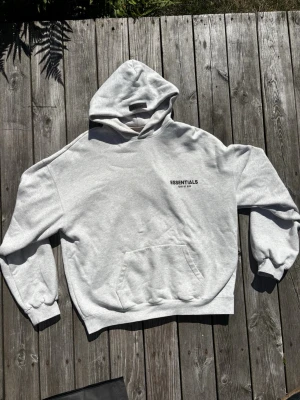 Essentials Fear of God hoodie - Säljer min grå hoodie från Essentials Fear of God model light oatmeal. Hoodien har en stor huva och magficka. Den är jätte skön att ha på sig, hade velat ha kvar den men har tyvärr blivit för stor då jag har gått ner i vikt.😥 Tillverkad i mjukt bomullsmaterial som är perfekt för en streetwear-look. Använd cirka 25 gånger.