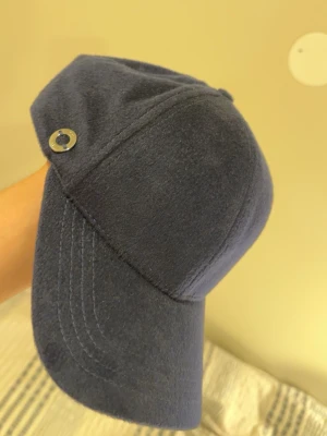 Cashmere keps - Snygg mörkblå keps från GOBI i 100% mongolisk kashmir. Klassisk form med böjd skärm och en liten metallknapp på sidan som detalj. Perfekt accessoar för dig som vill ha något stilrent och lyxigt till din outfit.