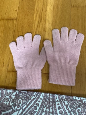 Ljusrosa stickade fingervantar för barn - Säljer ett par ljusrosa stickade fingervantar med ribbade muddar. Perfekta för kyliga dagar när du vill hålla händerna varma men ändå kunna använda mobilen. Snygg och enkel design som passar till det mesta.