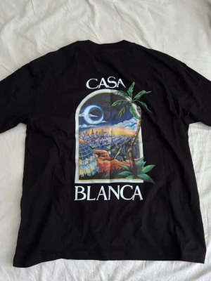 Svart Casablanca t-shirt - Snygg svart t-shirt från Casablanca med stort färgglatt tryck på ryggen och mindre tryck fram. Motivet visar en stadsvy med palmer och texten 'Casa Blanca'. Klassisk passform och rund hals. Perfekt för dig som vill sticka ut med stil.