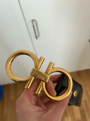 Svart skärp från Salvatore Ferragamo - Svart skärp från Salvatore Ferragamo med guldigt spänne i metall. Skärpet är gjort i äkta skinn och har flera hål för justerbar passform. Skärpet är 105cm. Pris kan diskuteras 
