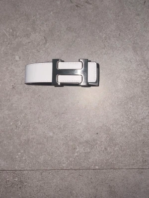 Vitt bälte - Ett vitt premiumläderbälte med en karakteristisk metallspänne som ger en exklusiv och sofistikerad touch till outfit