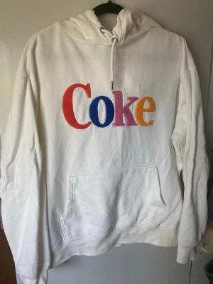 Krämvit hoodie med färgglad Coke text - Offwhite hoodie med text Coke på. Köpt på hm i collab med Coca Cola.