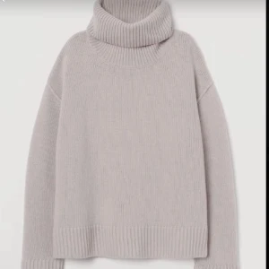 Beige polotröja i stickat - Mysig beige stickad polotröja med bred ribbad krage, muddar och nederkant. Tröjan har en avslappnad passform och långa ärmar, perfekt för kyliga dagar. Enkel och stilren design som passar till det mesta.