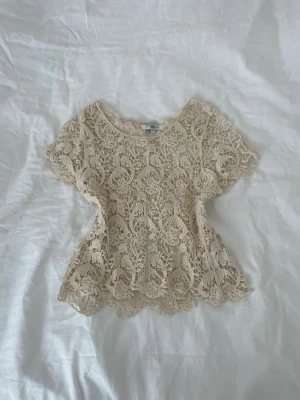 Beige spetsblus med volang - Säljer en superfin beige blus i spets med korta ärmar och volangkant nedtill. 