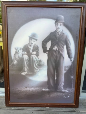 Tavla med svartvit motiv S. Coffield - Säljer en inramad tavla med svartvitt motiv av Charlie Chaplin i klassisk klädsel och en tigerunge. Tavlan har en brun träram och konstnären är S. Coffield. Perfekt som unik väggdekoration för dig som gillar retro och konst. Köpt år 2003