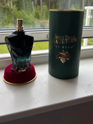  100ml Jean Paul Gaultier Le Beau Le Parfum - Jean Paul Gaultier Le Beau Le Parfum i en unik flaska formad som en manlig torso i svart och turkos glas med gulddetaljer. Kommer i en elegant grön cylinderförpackningmed guldfärgad text och dekor. Perfekt för dig som gillar exklusiva och stilrena dofter.