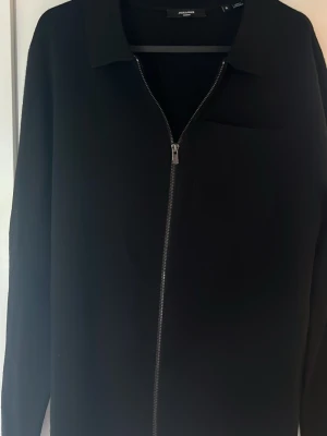 Svart overshirt från Jack & Jones - Stilren svart overshirt i storlek S från Jack & Jones med dragkedja framtill och klassisk krage. Tröjan är i nytt skick! Overshirten har en bröstficka och är tillverkad i ett mjukt tyg som passar perfekt för lager på lager. Funkar till det mesta. Skriv vid funderingar🤝