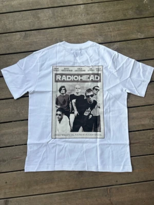 Radiohead vit t-shirt med tryck - Vit t-shirt med stort svartvitt tryck på ryggen som visar bandet Radiohead och texten 'I wish I was special you're so fuckin' special'. Klassisk passform och rund hals. Perfekt för dig som gillar bandmerch och vill sticka ut.