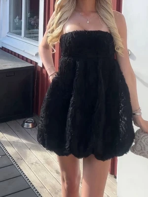Zara kort klänning - Säljer en svart axelbandslös kort klänning med puffig kjol och struktur i tyget. Klänningen har en ballongformad siluett och är perfekt för dig som vill sticka ut. Passar till många olika tillfällen och är riktigt trendig just nu.