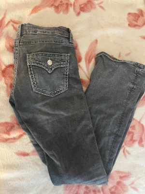 Grå jeans med detaljerade bakfickor - Säljer ett par grå jeans med snygga, detaljerade bakfickor och dekorativa sömmar. Jeansen har en tvättad look och raka ben. Perfekta för dig som gillar en avslappnad men ändå trendig stil.