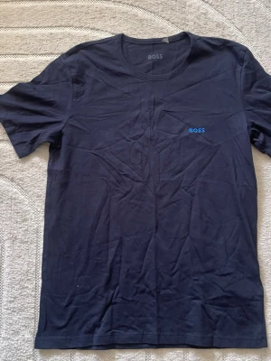 Mörkblå t-shirt från BOSS - Snygg mörkblå t-shirt från BOSS med diskret logga i blått på bröstet. Klassisk rund halsringning och korta ärmar. Tillverkad i mjuk bomull som känns skön mot huden. Perfekt basplagg för en clean och stilren look.