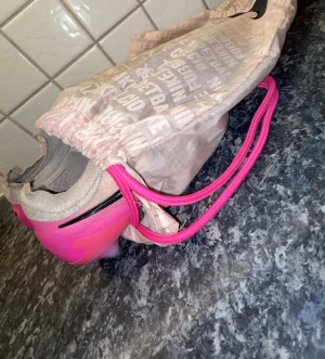 Nike Mercurial grå/rosa fotbollsskor - Säljer ett par Nike Elite Phantom i rosa och ljus aprikos färg som är i storlek 40, använda några gånger men fortfarande väldigt bra med snörning som gör så passformen blir ännu bättre. Du får även med en jättefin påse till skorna