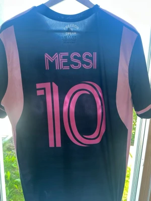Inter Miami Messi matchtröja - Snygg svart och rosa Inter Miami matchtröja från Adidas med Messi och nummer 10 på ryggen. Väldigt bra kvalite går inte sönder lätt. Stolek L men sitter L-M