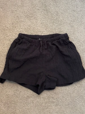 Svarta shorts med snörning i strl 146 från H&M. - Svarta shorts i mjukt, strukturerat tyg med elastisk midja och snörning framtill. Perfekta för varma dagar och har en avslappnad passform. Lätta att matcha med olika toppar.