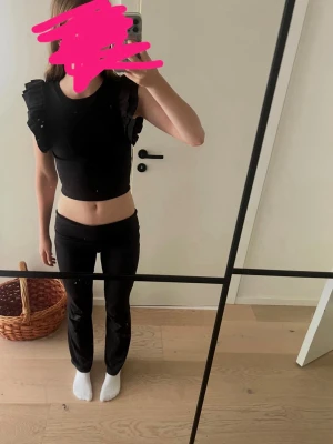 Svart topp med volangärmar - Snygg svart topp med markerade volangärmar som ger en cool och trendig look. Rund halsringning och rak passform. Perfekt att styla till både jeans och kjol för en chic outfit.