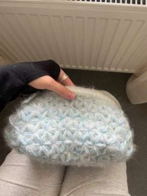 Ljusblå egenvirkad clutchbag - Superfin ljusblå clutchbag med fluffig, stickad yta och blommigt mönster. Väskan har ett mjukt foder i satinliknande tyg och stängs med en metallknäppning. Perfekt för dig som gillar unika accessoarer och vill sticka ut.