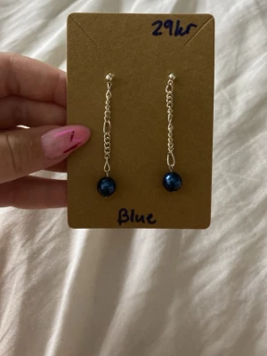 Silverörhängen med blå pärlor - Säljer ett par snygga örhängen med silverfärgade kedjor och blå pärlor längst ner. Örhängena är långa och hängande, perfekta för att ge en cool touch till din stil. Inget märke syns på bilderna.jag har gjort dom helt själv och alla örhängen är allergifria❤️