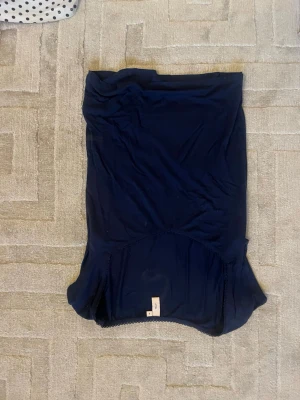 Marinblå axelbandslös klänning Nelly - Säljer en marinblå axelbandslös klänning från Nelly. Klänningen är kort och har en enkel, stilren design med diskret spetskant nedtill. Perfekt för dig som gillar minimalistisk stil och vill ha något bekvämt och snyggt.
